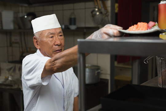 Senior chef holding plate of sushi in kitchen