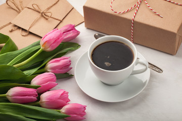 Pink tulips, a cup of coffee and a gift on a light stone background. Concept of Spring