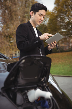 Man using digital tablet while charging electric car
