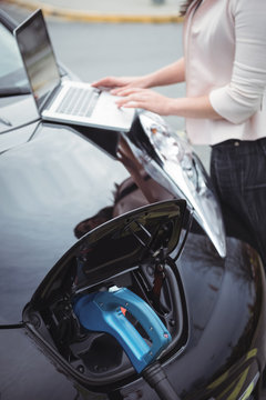 Mid section of woman using laptop while charging electric car