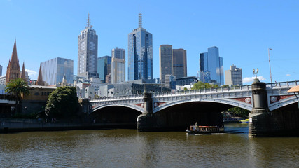 Naklejka premium Melbourne, Australia. Skyscrapers and the bridge over the Yarra river. Boat passes through the Princes Bridge