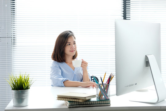 Young asian woman holding a coffee cup with smiling face, positive emotion at working desk background, casual office life, worink at home concept