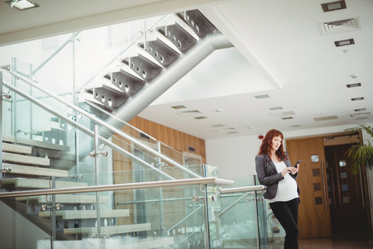 Pregnant businesswoman using mobile phone near staircase