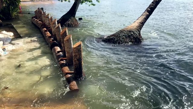 Waves crashing over a ruined boardwalk as rising seas take the shore of a rustic tourist beach in Bahia, Brazil