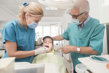 Obraz premium Boy with perfect teeth at the dentist doing check up with two doctors - oral hygiene health care concept