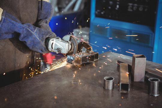 Welder cutting metal with electric tool in workshop
