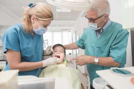 Boy with perfect teeth at the dentist doing check up with two doctors  - oral hygiene health care concept