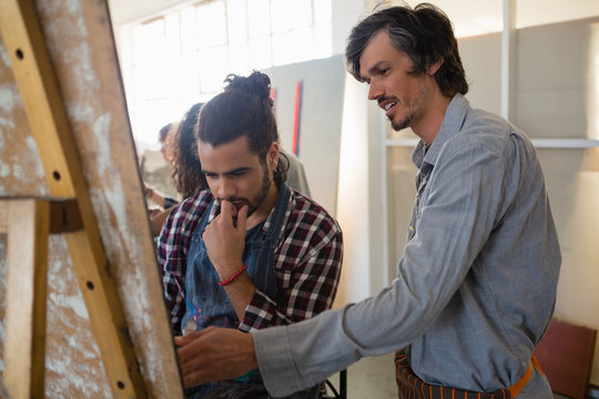Man assisting male friend while painting in art class