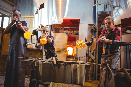 Team of glassblowers shaping a glass on the blowpip