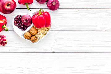 Diet for healthy heart. Food with antioxidants. Vegetables, fruits, nuts in heart shaped bowl on white wooden background top view copy space