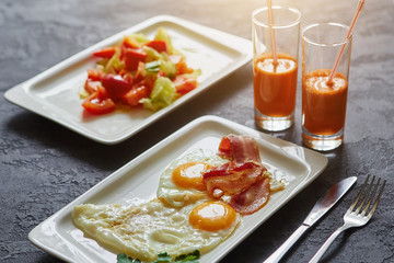Breakfast from fried egg, bacon, vegetable salad and carrot juice. On a dark stone background