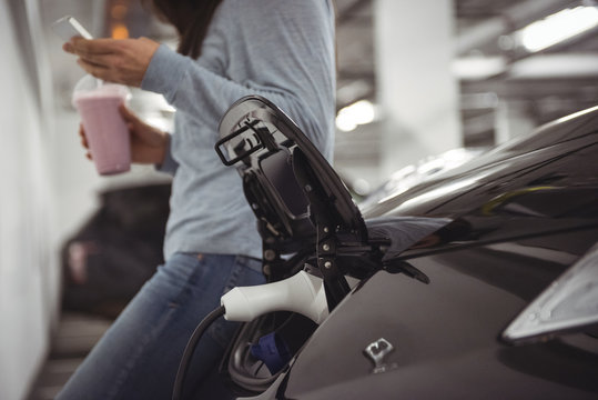 Car being charged with electric car charger while woman standing in background 