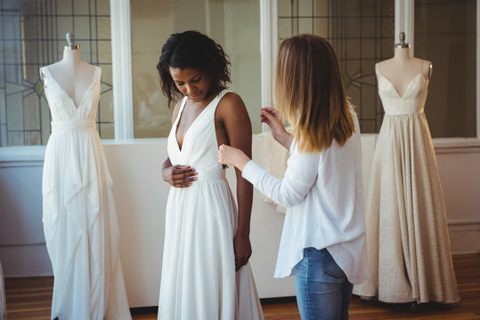 Woman trying on wedding dress with the assistance of fashion designer