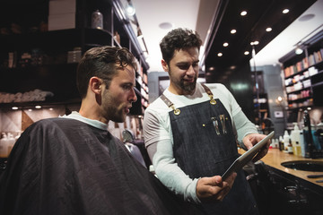 Barber showing hairstyle to client on digital tablet