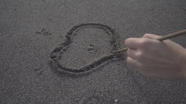 Girl on a beach draws a hearts on sand. Girl drawing heart symbol on sand beach