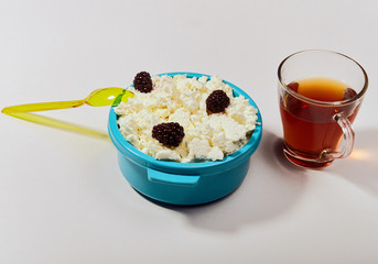 Blue plate with cottage cheese with a yellow spoon and a cup of tea on a light background in the studio