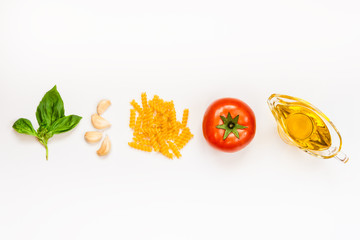 Top view of pasta ingredients over white background - raw fusilli, fresh basil, garlic cloves, olive oil and ripe tomatoe. Italian food minimal concept.