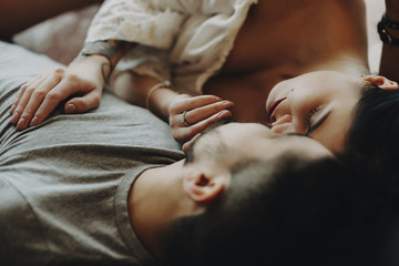 Seductive adult couple laying on bed and hugging with closed eyes.