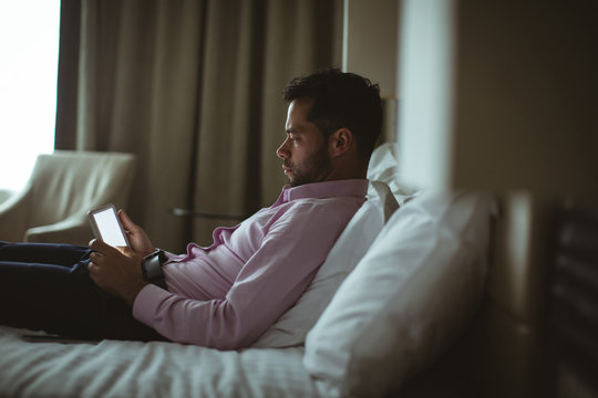 Businessman using digital tablet while relaxing on bed at home