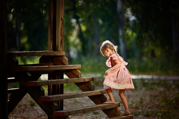 beautiful little girl with funny face expressions playing, climbing up on a wooden stairs