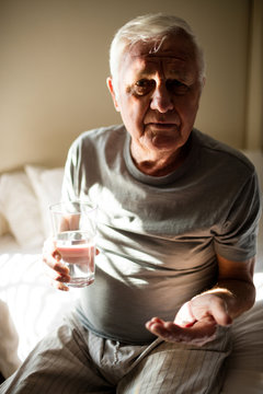 Senior man taking medicine in the bedroom