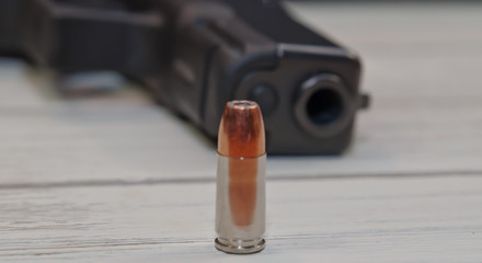 A single 9mm hollow point bullet on a white table in front of a black pistol