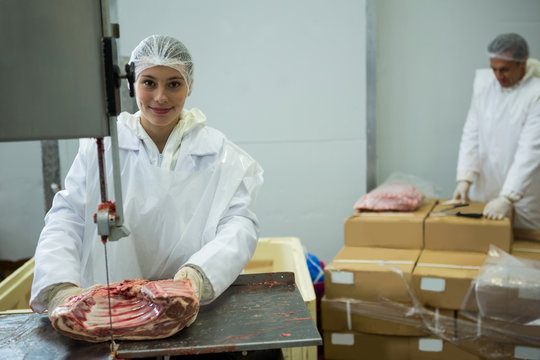 Female butcher cutting meat with meat cutting machine