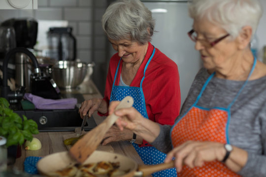  Senior friends cooking food together in kitchen