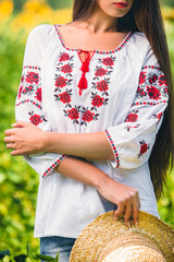 girl is standing in embroidered blouse with patterns and a hat in her hand