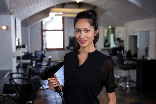 Smiling female hairdresser holding brush in hair salon