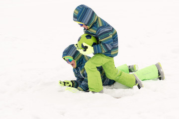 Fototapeta na wymiar A young lady in a blue ski suit plays football with children in the snow. Yellow sled, sunglasses, bright clothes. Girl happy outdoors. Fun winter vacation for the whole family. Green soccer ball