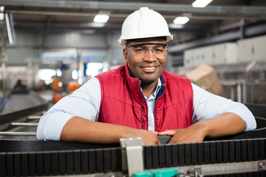 Smiling male employee standing by conveyor belt in factory