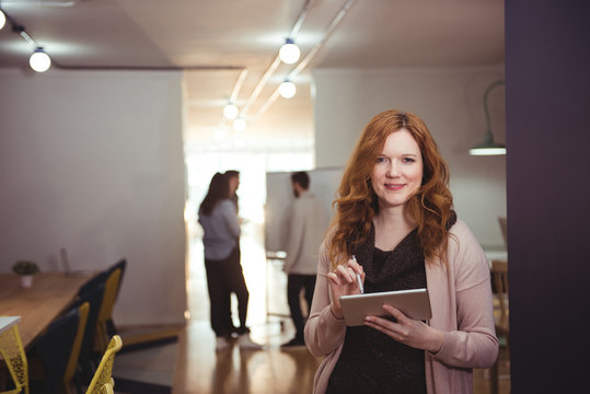 Portrait of smiling young woman with digital tablet standing indoors