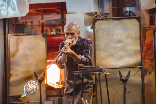 Glassblower shaping a glass on the blowpipe
