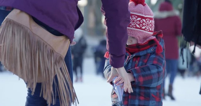 Mother helps toddler boy get snack out of bag at outdoor winter festival