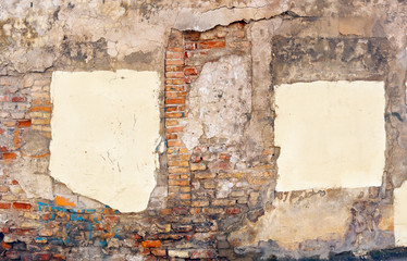 A piece of the wall of the ruined house with paint stains and yellow plaster patches that close the windows.