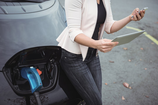 Mid section of woman using mobile pone while charging electric car