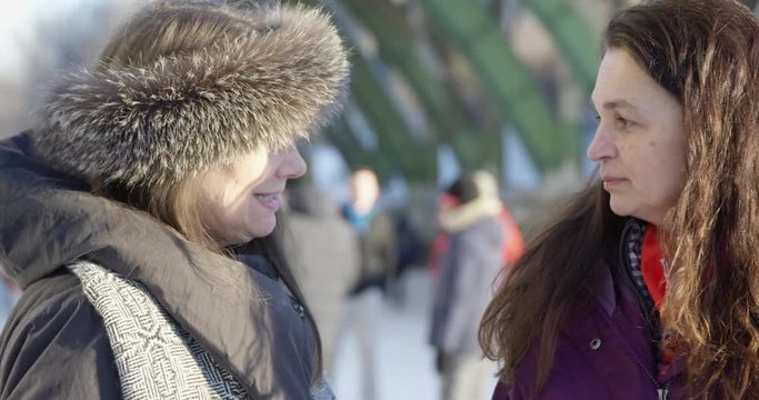 Older woman turns to talk to friend outdoors in winter