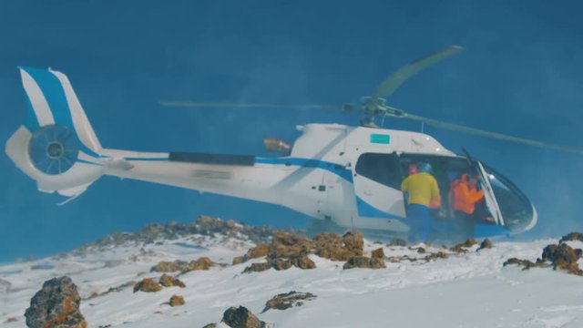 The helicopter landed in the mountains in winter, raising a cloud of snow
