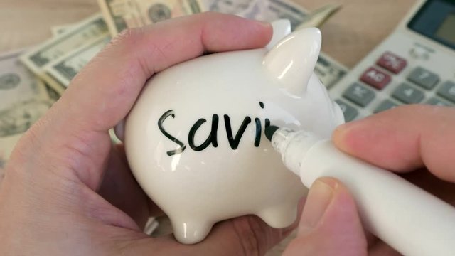 Hands writing savings tips on a piggy bank.