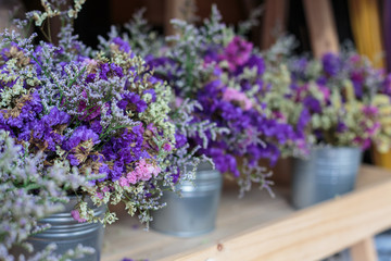 Violet dried flowers in blue tin watering flower pot on wooden table background.