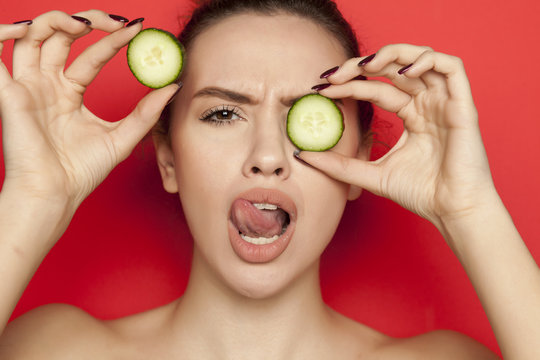 Sexy young woman posing with slices of cucumber on her face on red background