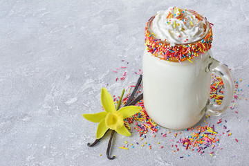 Crazy vanilla milk shake with whipped cream and colored sprinkles in glass jar
