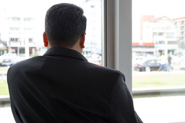 Fototapeta premium businessman in black suit looking out from window