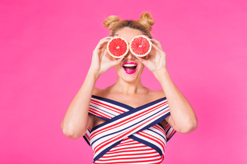 Beauty Model Girl takes Juicy Grapefruit. Beautiful Joyful young girl, funny blonde hairstyle and pink makeup.Holding Orange Slices and laughing, emotions.