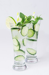 Fresh detox cocktail of cucumber, lime, mint, straw with bubbles, drops on soft white wooden backgrouns. Dieting spring cold drink.