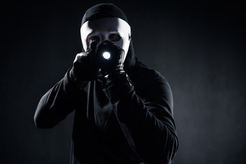 Burglar in mask and balaclava aiming with gun and flashlight