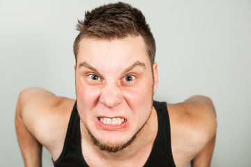 Fototapeta premium Young funny bearded guy dressed in black tank top sitting on the toilet on gray background.