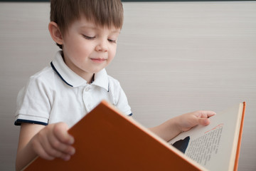 A cute child is reading a book. The boy looks with interest in the book.