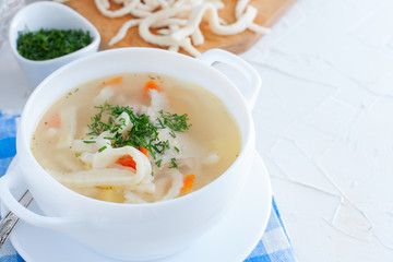 Chicken soup with homemade noodles in a white ceramic soup plate on a white table, horizontal, copy space